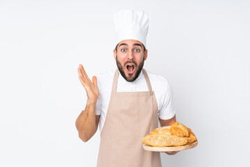 Male baker holding a table with several breads isolated on white background with surprise facial expression