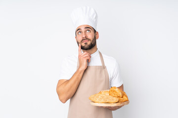 Male baker holding a table with several breads isolated on white background thinking an idea