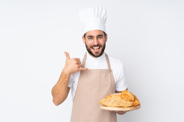 Male baker holding a table with several breads isolated on white background making phone gesture