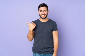 Caucasian handsome man pointing to the side to present a product over isolated purple background