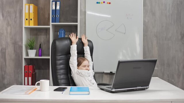 A portrait of a small cute child depicting the head of the agency at a white table, stretching from fatigue. In the background is a bookcase with accounting records. The concept of adult children.