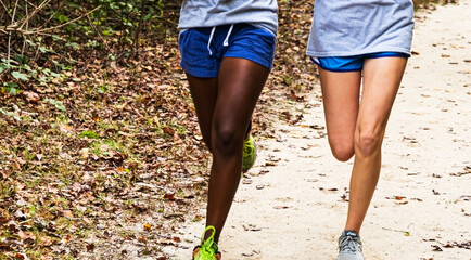 Legs of two girls running side by side on a dirt path