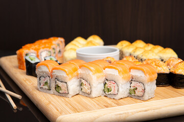 Big sushi set on light wooden dish isolated on black background