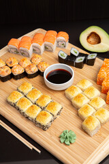 Big sushi set on light wooden dish isolated on black background