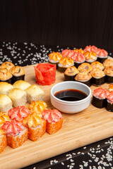 Big sushi set on light wooden dish isolated on black background