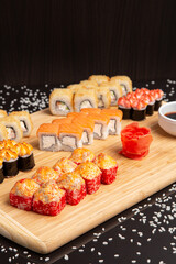 Big sushi set on light wooden dish isolated on black background