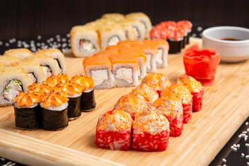 Big sushi set on light wooden dish isolated on black background