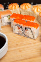 Big sushi set on light wooden dish isolated on black background