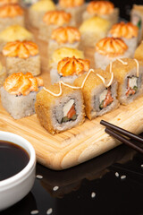 Big sushi set on light wooden dish isolated on black background