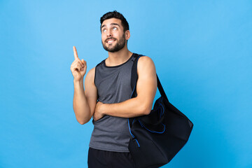 Young sport man with sport bag isolated on blue background pointing up a great idea