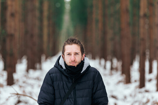 Handsome young man standing in a snowy forest looking straight into the camera