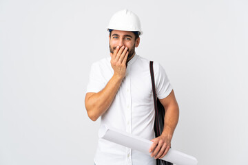 Young architect man with helmet and holding blueprints isolated on white background happy and smiling covering mouth with hands
