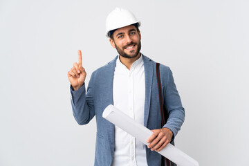 Young architect man with helmet and holding blueprints isolated on white background showing and lifting a finger in sign of the best