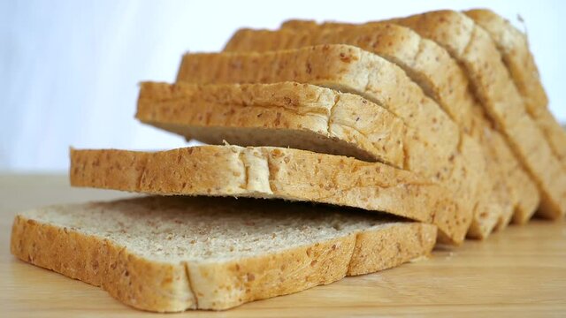 Close up slow motion of falling whole wheat bread sliced on wooden table
