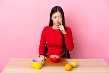 Young Chinese girl  having breakfast in a table frustrated and pointing to the front