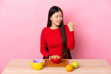 Young Chinese girl  having breakfast in a table pointing to the side to present a product