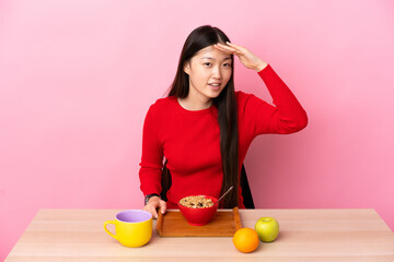 Young Chinese girl  having breakfast in a table looking far away with hand to look something
