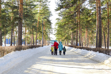 Fototapeta na wymiar A family with children walks in a winter park on a sunny day. Bright winter landscape. Family joint outdoor recreation. Copy space.