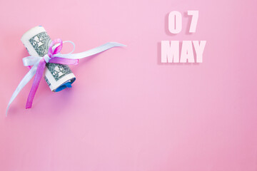 calendar date on pink background with rolled up dollar bills pinned by pink and blue ribbon with copy space. May 7 is the seventh day of the month
