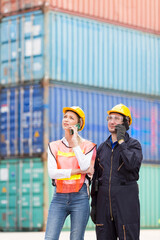 The supervisor wearing a safety suit is controlling the movement of goods in the container by using radio communication. Engineers are using mobile phones in the port of loading goods.