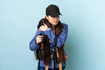 Young Chinese girl with backpack and trekking poles over isolated blue background suffering from pain in shoulder for having made an effort