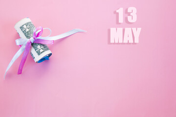 calendar date on pink background with rolled up dollar bills pinned by pink and blue ribbon with copy space. May 13 is the thirteenth day of the month