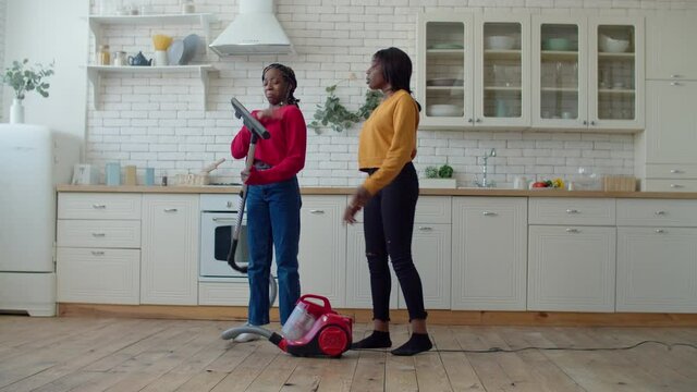 Confused annoyed attractive african teenage girls doing household chores and arguing, trying to fix broken vacuum cleaner, being puzzled and irritated while doing housework together at home.