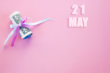 calendar date on pink background with rolled up dollar bills pinned by pink and blue ribbon with copy space. May 21 is the twenty first day of the month