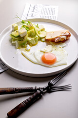 Delicious and healthy breakfast. Fried egg and vegetable salad with avocado and herbs. Mini croissant with ham and cheese on a round white plate. Organic food. Vertical shot