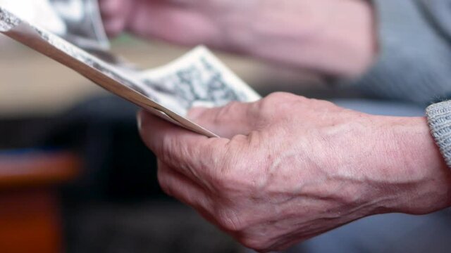 Memories of an elderly man looking at old photographs. Close up of hand of pensioner holding family photo. Nostalgia for the past years. Selective focus, shallow depth of field