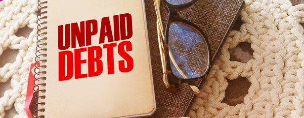 Unpaid debts words on copybook, glasses, pen. Financial obligations concept