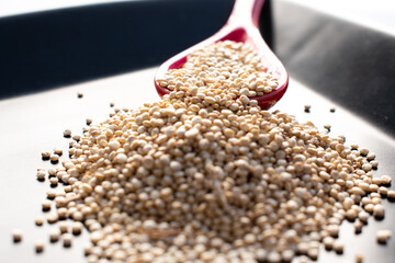 Quinoa in a red ceramic spoon on a black dish, isolated