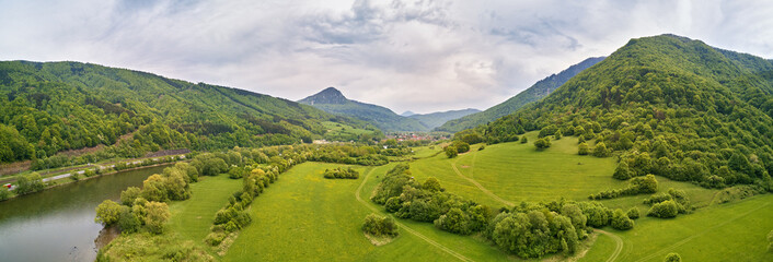 Village, river and road in mountain valley. Green mountain meadows and hills. Kraľoviansky meander on river Bar. Spring panorama