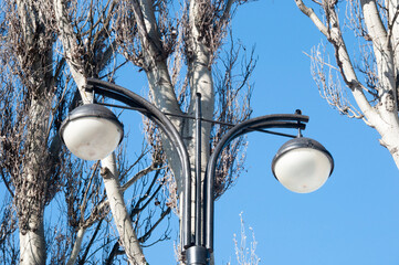 Lighting pole with round lamps on the background of trees and blue sky.