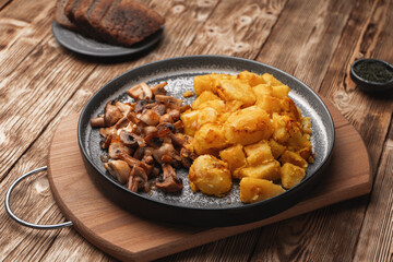 A plate of fried potatoes with mushrooms on a plank wooden table