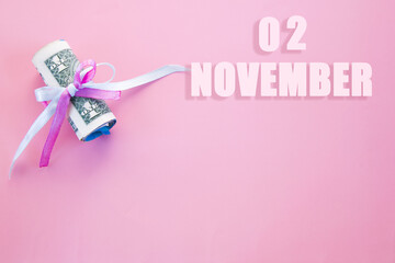 calendar date on pink background with rolled up dollar bills pinned by pink and blue ribbon with copy space.  November 2 is the second  day of the month