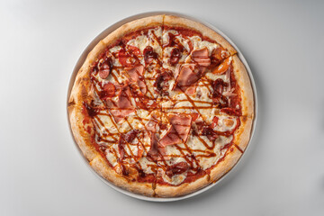 Meat pizza with sausage with a high side on a white plate, top view