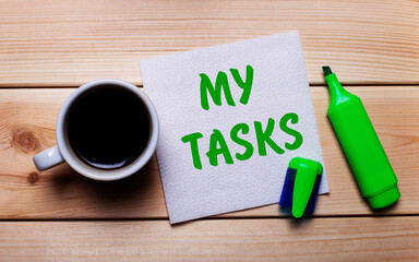 On a wooden table, a cup of coffee, a green marker and a napkin with the text MY TASKS