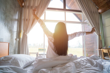 Beautiful asian women is waking up in the morning, Stretches in the Bed, Sun Shines on Her From the...