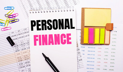 A notebook with the words PERSONAL FINANCE, a marker, colored paper clips and bright note paper lie on the background of the graphs.