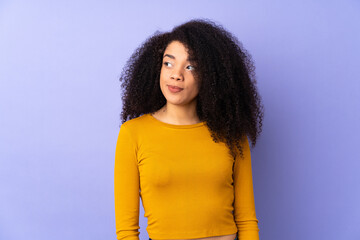 Young african american woman isolated on purple background making doubts gesture looking side