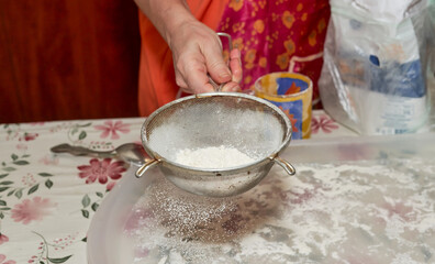 Woman sifts flour through a sieve on a white tray
