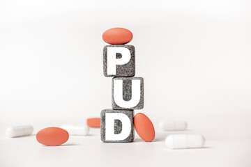 a group of white and red pills and cubes with the word PUD Peptic ulcer disease on them, white background. Concept carehealth, treatment, therapy.