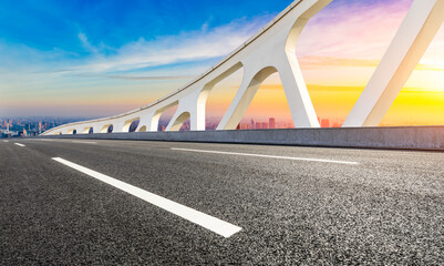 Asphalt road and city skyline at sunset in Shanghai.