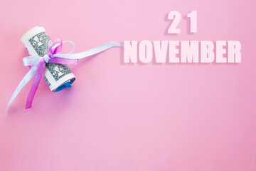 calendar date on pink background with rolled up dollar bills pinned by pink and blue ribbon with copy space. November 21 is the twenty first day of the month