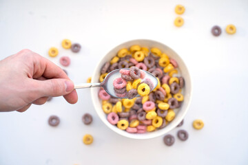 A man's hand holds a spoon with colored flakes on a white background.