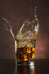 Dropping ice cubes into a whiskey glass on a wooden background