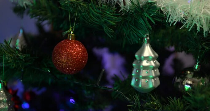 Blinking blue lights on a christmas tree between hanging decorative bubbles close up
