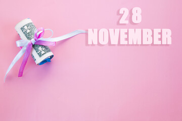 calendar date on pink background with rolled up dollar bills pinned by pink and blue ribbon with copy space. November 28 is the twenty-eighth day of the month