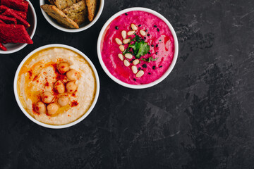 Beet hummus and classic hummus with crisp bread in bowls on dark stone background.